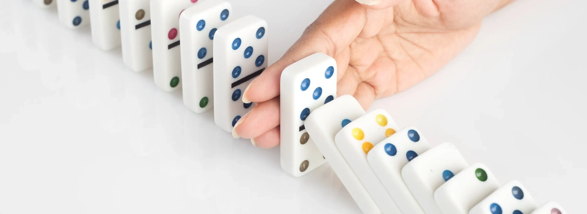 Dominoes falling but stopped by a hand.